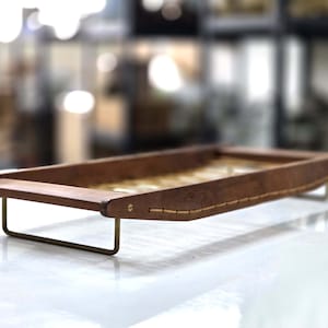 Op de afbeelding: Een houten dienblad met een geweven ontwerp en messing poten. Het dienblad is gemaakt van donker hout en heeft een natuurlijke afwerking.