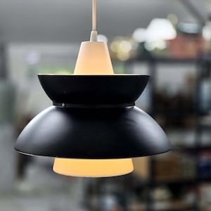 May include: A black and white pendant light with a white frosted glass shade. The light has a modern design with a layered, tiered shade.