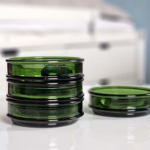 Può includere: Quattro portacandele in vetro verde impilati con un singolo portacandele in vetro verde sul lato destro dell'immagine.