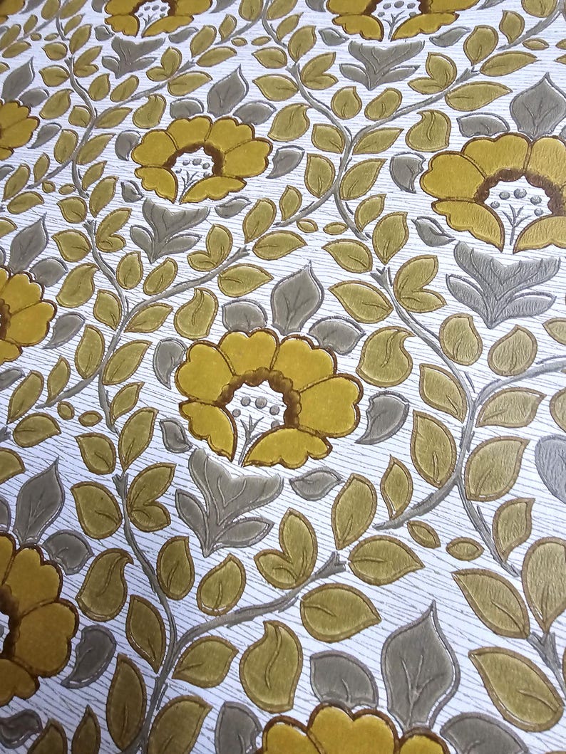 May include: Wallpaper featuring a repeating floral pattern with mustard yellow flowers and sage green leaves on a white background. The design includes embossed textures that create a raised effect for the petals and foliage across the surface.