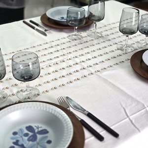 May include: A white tablecloth with a brown and white pattern is set for a dinner party. There are six wine glasses, two plates, and two forks on the table.