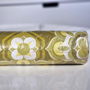 May include: A roll of wallpaper wrapped in clear plastic film, featuring a repeating geometric pattern in shades of olive green, lime green, and white. The design consists of stylized floral shapes and interlocking hexagonal outlines.