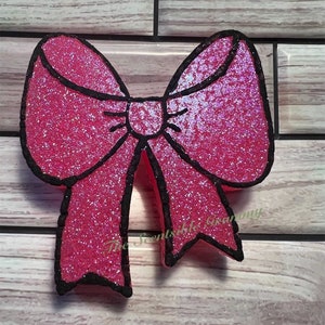 May include: A pink glitter bow with a black outline. The bow is a decorative item.