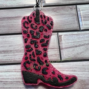 May include: Pink cowboy boot shaped car air freshener with a black leopard print design. The boot is hanging from a black string.