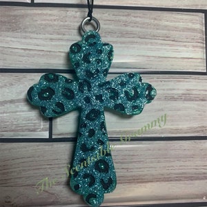 May include: Teal blue cross with a black leopard print design and glitter. The cross is a hanging ornament with a black string.