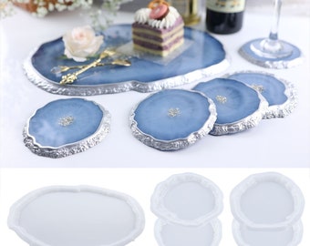 May include: A set of blue and silver resin coasters and a serving tray. The coasters and tray have a silver trim and a blue, agate-like design. A cake and wine glass are also visible.