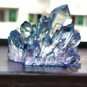 May include: A cluster of blue and purple crystals with sharp, pointed edges. The crystals are arranged in a dense formation, creating a textured surface. The color transitions from a deep purple at the base to a light blue at the tips, with hints of iridescence.