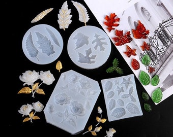 May include: An assortment of leaf and flower molds and resin castings. The molds are light blue and feature various leaf and flower designs. The resin castings are in shades of red, green, gold, and white. The word "BREAK" is visible on a white paper.