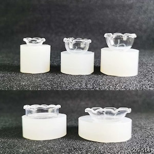 May include: Several clear glass miniature bowls with scalloped edges are presented on white pedestals. The small bowls have a delicate, transparent appearance. The arrangement showcases the bowls from different angles, highlighting their design.