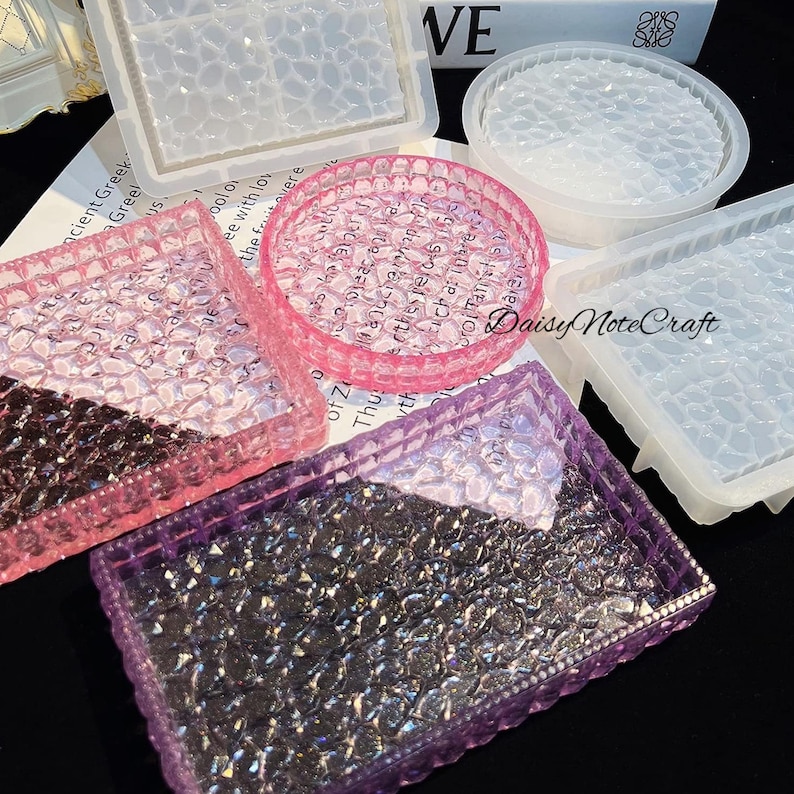 May include: A collection of resin molds in various shapes, including square, rectangular, and circular designs. The molds are in clear, pink, and purple hues, with a textured, bubble-like pattern. The image also shows the text "Daisy Note Craft".