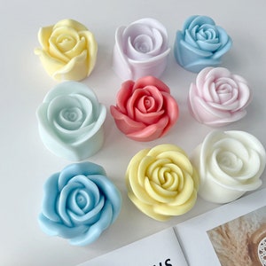 May include: Nine rose-shaped objects in pastel shades of yellow, pink, blue, and white. The objects are arranged on a white surface, highlighting their detailed petal structures. The image suggests a floral or decorative theme, possibly for crafts or home decor.