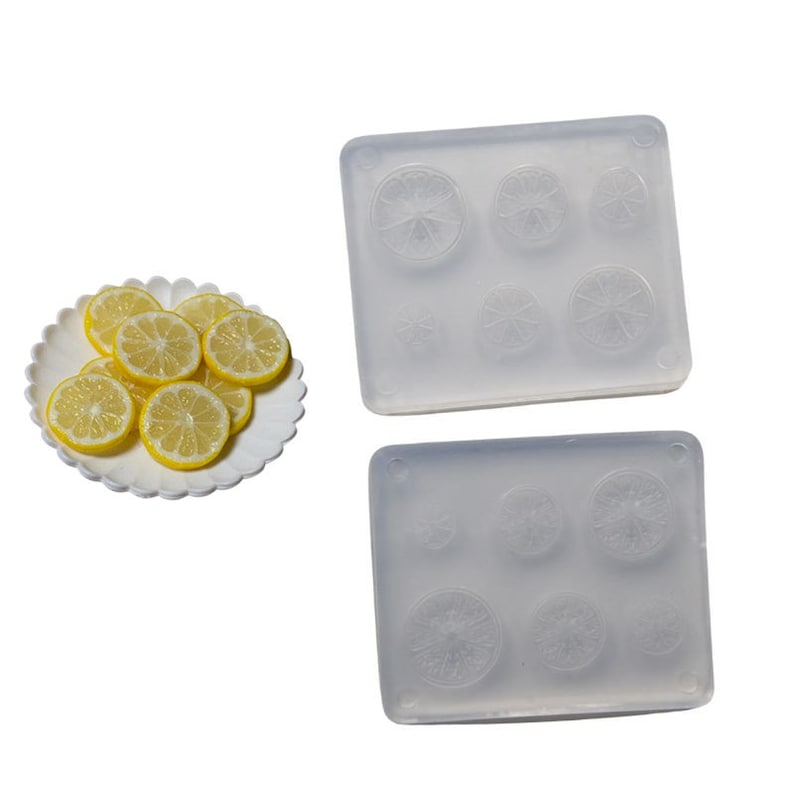 May include: A white plate holds several yellow lemon slices. Two clear silicone molds with lemon slice impressions are also shown. The molds have various sized circular cavities for creating lemon-shaped items.