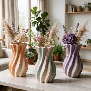 Può includere: Tre vasi in ceramica con un design a spirale e scanalato. Il vaso a sinistra è color pesca e bianco, quello centrale è verde pastello e rosa, e quello a destra è viola e bianco. Ogni vaso contiene un bouquet di fiori secchi ed erba della pampa.