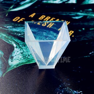 May include: A transparent, geometric silicone mould in a diamond shape. The mould has a wide opening and tapers to a point at the base. The text "MOLDTIME" is visible on the base of the mould.