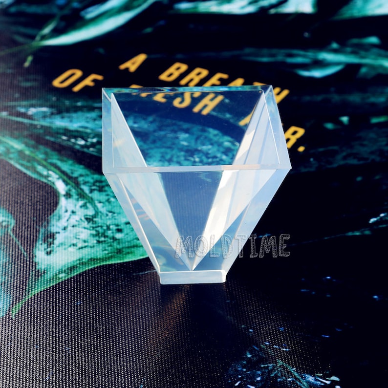 May include: A transparent, geometric silicone mould in a diamond shape. The mould has a wide opening and tapers to a point at the base. The text "MOLDTIME" is visible on the base of the mould.