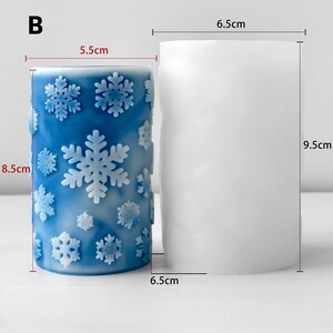 May include: A blue candle with snowflake designs, measuring 8.5cm high and 5.5cm in diameter, next to a white candle mould, 9.5cm high and 6.5cm in diameter. The candle has a winter theme.