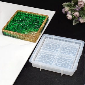 May include: Square resin tray with a green and gold design. The tray has a textured surface with a gold glitter border. A clear silicone mold with a leaf pattern is next to the tray.