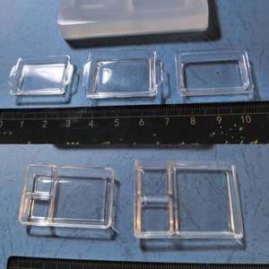 May include: Clear silicone moulds for crafting. The image shows several small, clear trays with varying designs, including some with handles and divided compartments. A ruler is included for scale, showing the moulds are small.