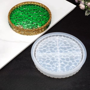 May include: A round, green and gold resin coaster with a textured surface. The coaster has a gold glitter border. A clear, round silicone mold with a pebble design is also shown.