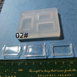 May include: A clear silicone mould with three rectangular cavities and three small, clear rectangular trays. The mould has the text "02#" printed on it. A ruler is at the bottom of the image.