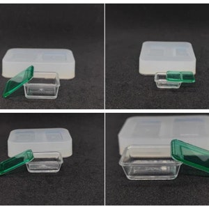 May include: A clear plastic container with a green lid, next to a larger, rectangular, white silicone mould. The container is rectangular and has a matching lid. The silicone mould has two rectangular cavities.
