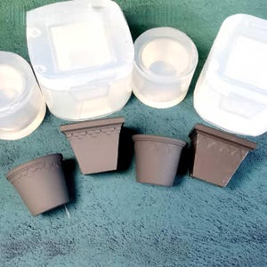 May include: An overhead shot shows several clear silicone molds and four small, gray, decorative flower pots. The pots have a scalloped design around the rim. The molds are in various shapes, including square and round.
