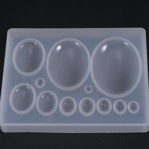 May include: A clear, rectangular silicone mold with various sized, rounded cavities. The mold features a variety of circular and oval shapes, perfect for resin casting or crafting projects. The cavities range in size from small circles to large ovals.
