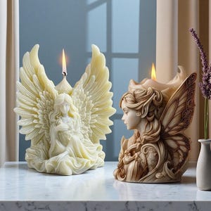Puede incluir: Dos velas con temática de ángeles y hadas. La vela de ángel es de color marfil con alas grandes y detalladas y una figura sentada. La vela de hada es de color marrón claro con el perfil de un hada con alas detalladas. Ambas velas tienen mechas encendidas.