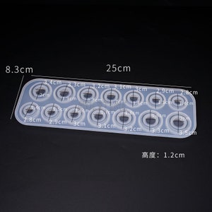 May include: A clear silicone mold with 14 circular cavities of varying sizes, designed for crafting. The mold is rectangular, measuring 25 cm long and 8.3 cm wide, with a height of 1.2 cm. Each circle's diameter is labeled in centimeters.