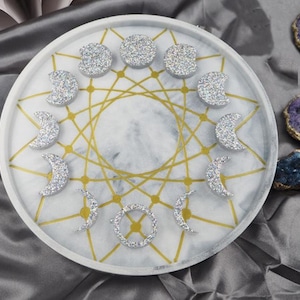 May include: A circular white tray with a marble effect, gold geometric pattern, and sparkling moon phase shapes. The tray is decorated with silver glitter crescent moons and circles.