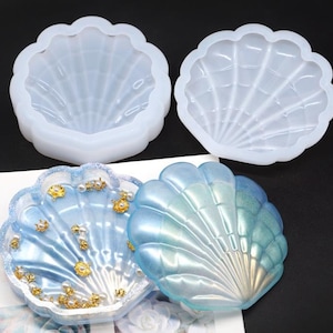 May include: Four seashell-shaped molds and two finished resin seashell trays. The molds are white and translucent. The finished trays are blue and decorated with gold and pearl accents. The trays are approximately 5 inches in diameter.