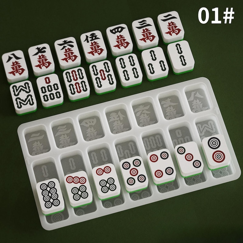 May include: A set of white and green Mahjong tiles with red and black markings, arranged on a clear plastic tray. The tiles feature Chinese characters and circular patterns. The background is a solid green color.