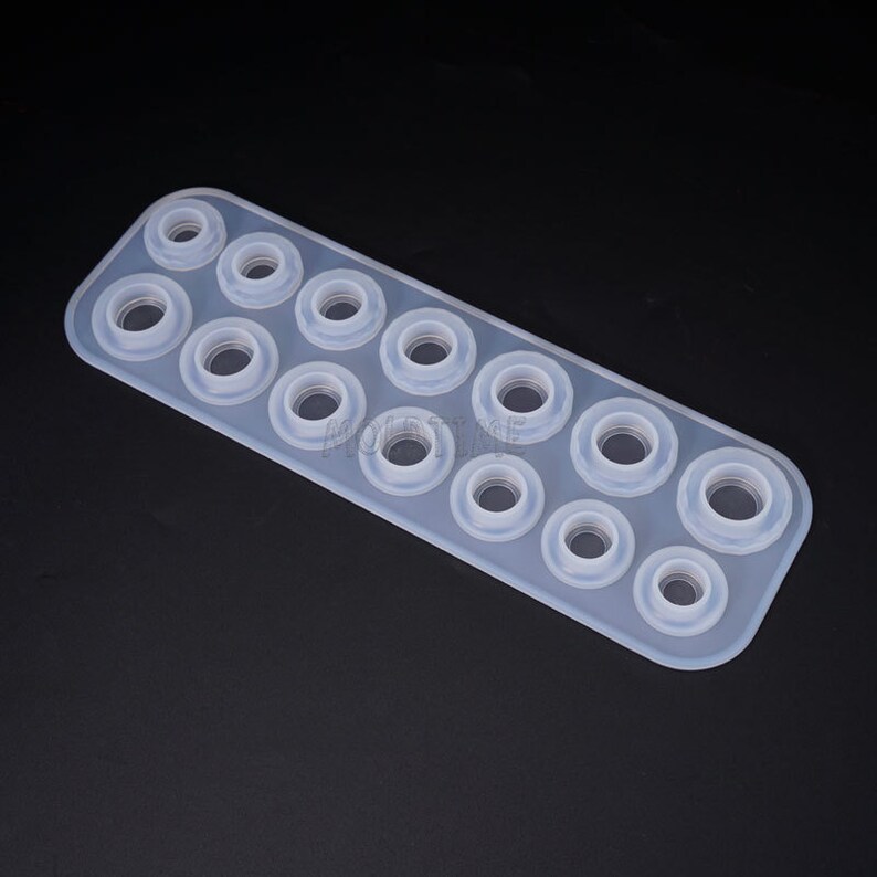 May include: A clear, rectangular silicone mold with multiple circular cavities of varying sizes. The mold is designed for crafting small, round objects, likely for jewelry or decorative purposes. The background is a solid black.