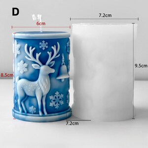 May include: A blue candle with a deer and snowflake design, measuring 8.5 cm high and 7.2 cm in diameter. The candle has a deer and bell relief, and a white wick. A second, unlit candle is also shown.