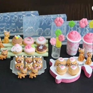 May include: A selection of miniature cat figurines, donuts, cupcakes, and pink-frosted drinks. The image also includes moulds for making paw-shaped and flower-shaped decorations. The items are arranged on a dark surface.