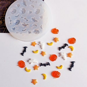 May include: A clear silicone mould featuring Halloween shapes like stars, moons, ghosts, bats, and pumpkins. There are orange, yellow, and black resin Halloween embellishments, ideal for crafting. The mould is for creating decorations.
