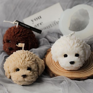 May include: Three dog-shaped candles in brown, cream, and white, with black eyes and noses. One candle has a wick. A white card with the words "YOU are beautiful" is in the background.