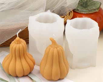 Peut inclure: Deux bougies orange en forme de citrouille avec des mèches blanches sont placées devant deux moules blancs en forme de citrouille. Une petite citrouille orange et un panier en osier sont en arrière-plan. Les bougies et les moules sont pour les décorations d'automne.