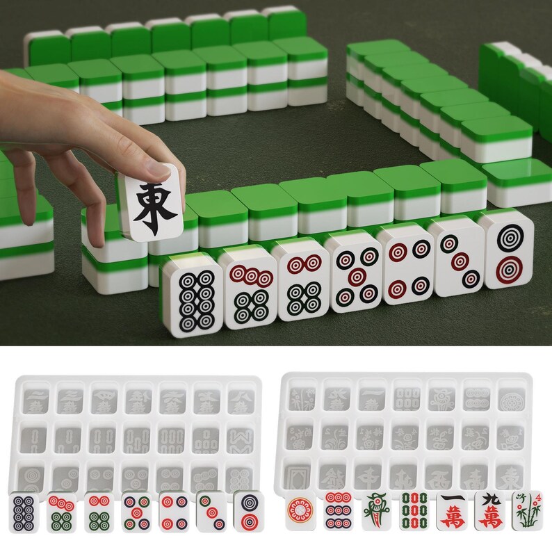 May include: A complete Mahjong set with green and white tiles, arranged on a green surface. The set includes tiles with various symbols and numbers, and two trays for storage. One tile is being held up, displaying a black character.