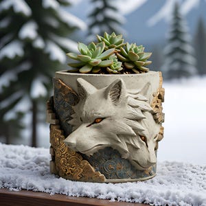 May include: A cylindrical concrete planter featuring a relief sculpture of two wolf heads with glowing orange eyes. The exterior is decorated with gold and blue patterned accents. A green succulent plant is potted inside the container.