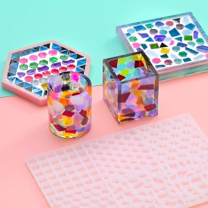May include: A collection of colorful mosaic art pieces, including a hexagonal coaster, a square container, a cylindrical cup, and a square tray. The pieces are made with various colored glass and resin. A white silicone mold is in the foreground.