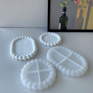 Peut inclure: Quatre plateaux décoratifs blancs de différentes formes : ronds, ovales et circulaires. Chaque plateau présente un bord perlé. Les plateaux sont faits d'un matériau lisse et opaque et sont disposés sur une surface blanche.