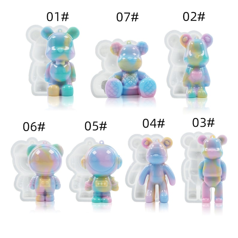 K&ouml;nnte beinhalten: Eine Sammlung farbenfroher B&auml;renfiguren aus Kunstharz in verschiedenen Posen. Die B&auml;ren sind haupts&auml;chlich in Pastellt&ouml;nen von Blau, Rosa und Gelb gehalten und haben ein gl&auml;nzendes Finish. Einige haben eine Schlaufe zum Aufh&auml;ngen. Das Bild zeigt einen Astronauten-B&auml;ren und einen sitzenden B&auml;ren.