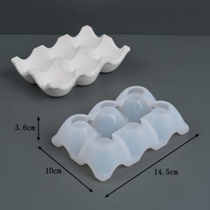 May include: Two egg-shaped moulds. One is white, the other is translucent. The white mould is 3.6 cm high. The translucent mould is 14.5 cm long and 10 cm wide. Both moulds are designed to hold six eggs.
