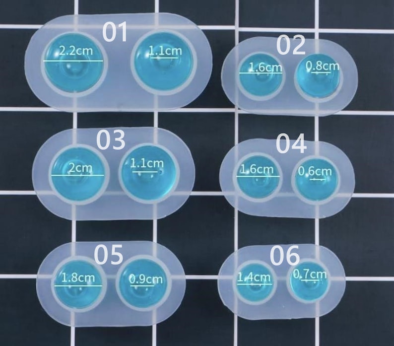May include: A clear silicone mold with six sets of two circular cavities. Each set is labeled with a number and has measurements in centimeters. The cavities are filled with a light blue resin. The largest cavity is 2.2cm.