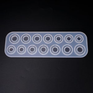 May include: A clear, rectangular silicone mold with 14 circular cavities of varying sizes. The mold is designed for crafting resin or other materials into circular shapes. The cavities are arranged in two rows, with the largest circles at the center.