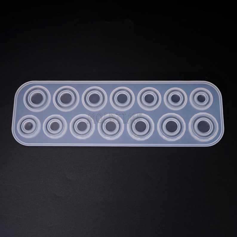 May include: A clear, rectangular silicone mold with 14 circular cavities of varying sizes. The mold is designed for crafting resin or other materials into circular shapes. The cavities are arranged in two rows, with the largest circles at the center.