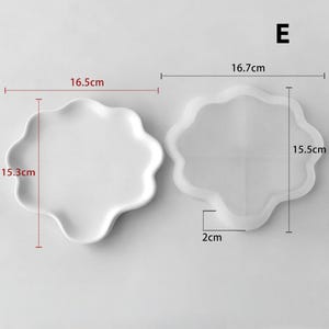 May include: Two white, wavy-edged plates. One plate measures 6.5 inches by 6 inches. The other plate is a clear, wavy-edged mold, measuring 6.6 inches by 6.1 inches, with a 0.8-inch depth. The letter "E" is in the upper right corner.