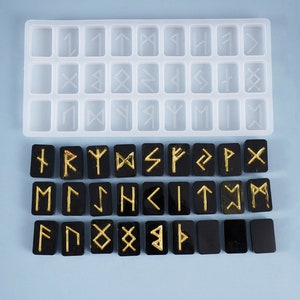 May include: A set of black resin rune stones with gold-colored symbols, displayed next to a clear silicone mold. The runes are rectangular and feature various ancient Norse alphabet characters. The mold has 24 rectangular slots.