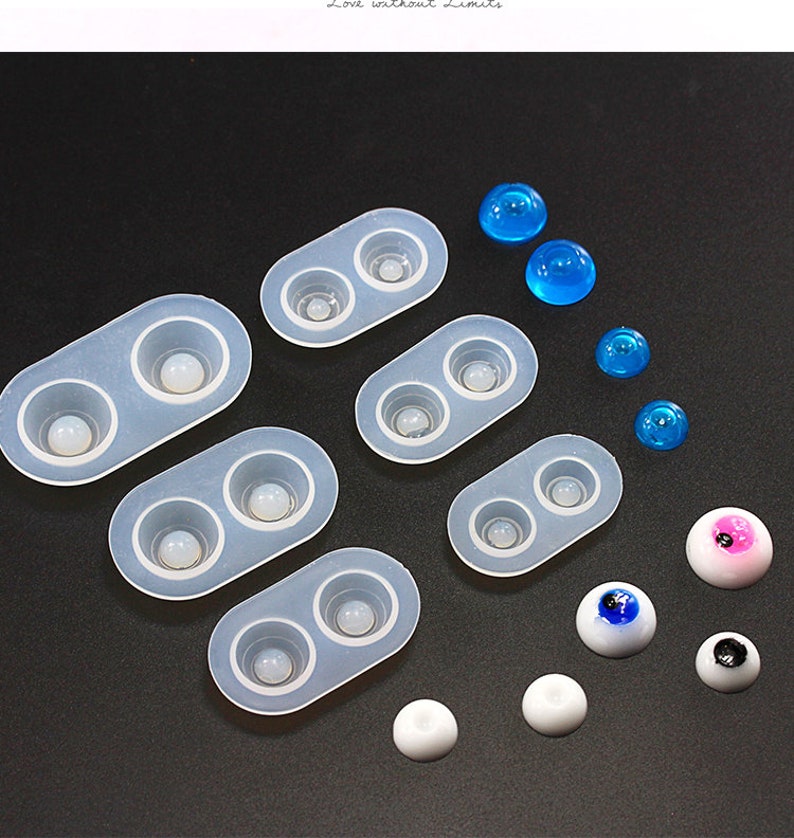 May include: A collection of silicone molds for crafting doll eyes, along with various finished eye pieces. The molds are translucent, and the finished eyes are white, blue, and pink. Some eyes have black pupils.